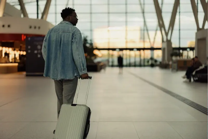 Rückansicht eines Reisenden mit Koffer in einem großzügigen, modernen Flughafen – Reisebeginn und Abflugkonzept