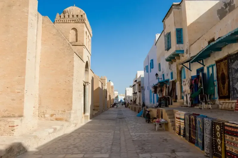 A street scene of Kairouan. On left side Great Mosque of Kairouan on right side shops with local products, Tunisia
