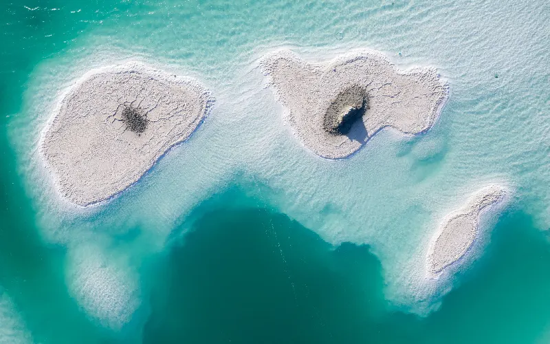 Aerial view of salt formations in turquoise water at the Dead Sea, creating a surreal landscape.