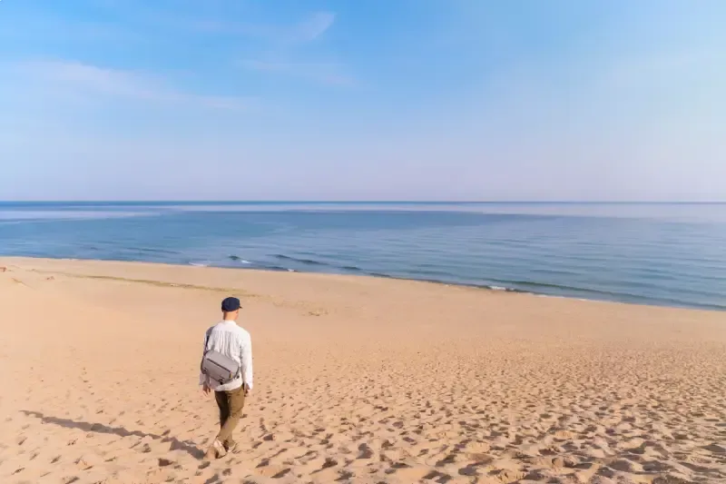 homem-caminhando-pelas-extensas-dunas-de-areia-de-tottori-no-japao-com-vista-para-o-mar-calmo-sob-um-ceu-azul-claro