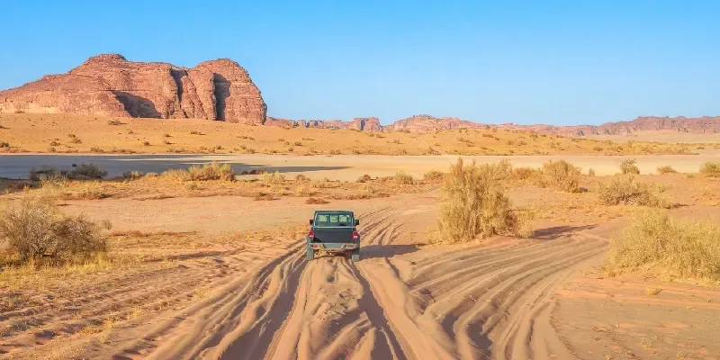 Un vehículo 4x4 recorre un camino de tierra entre imponentes formaciones de arenisca en la Reserva Natural de Sharaan, en AlUla, Arabia Saudita