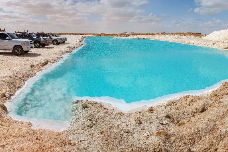 Salzbecken in der Siwa-Oase, Ägypten, mit kristallklarem türkisfarbenem Wasser, umgeben von weißen Salzrändern und Wüstenlandschaft