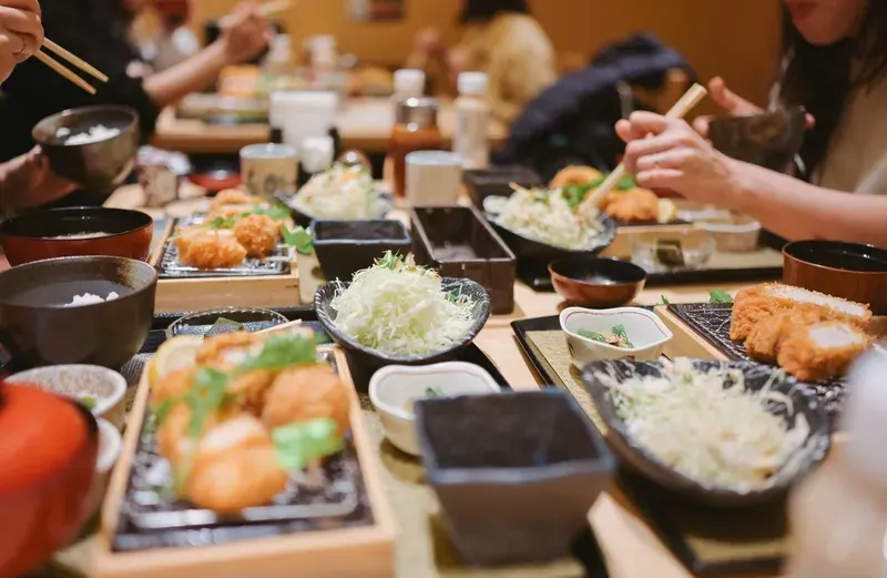 mesa-de-restaurante-japones-com-pratos-tipicos-e-pessoas-comendo-com-hashi