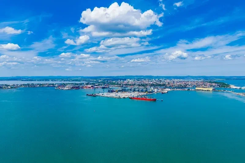 Leuchtend blauer Himmel über einem geschäftigen Hafen mit Schiffen, Kränen und einer Stadt an der Küste in Ägypten