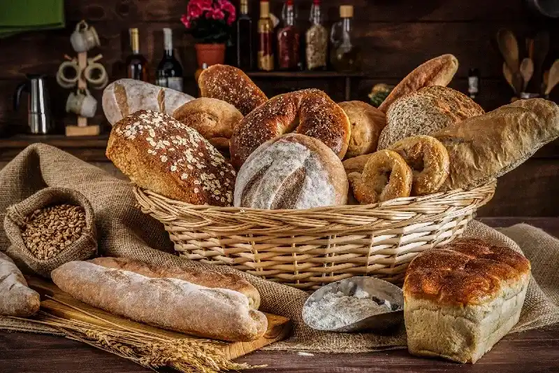 Gruppe von frischen gemischten Broten, Brötchen und Zutaten in einer rustikalen Küche.