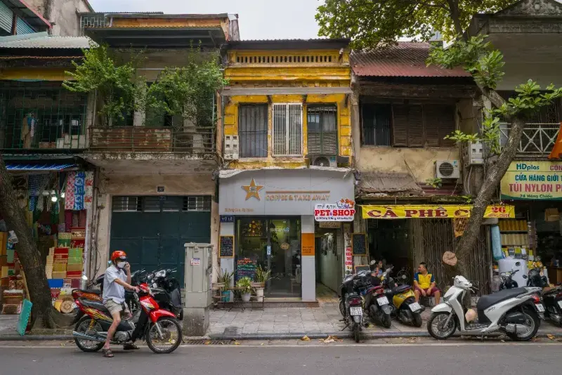 Escaparates con letreros, motocicletas estacionadas y gente a lo largo de la calle Hang Chieu, Hanói, Vietnam.