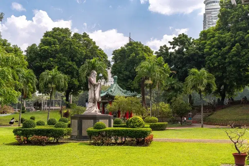 white-statue-of-confucius-standing-among-trimmed-hedges-with-a-traditional-chinese-pagoda-pavilion-rizal-park-manila