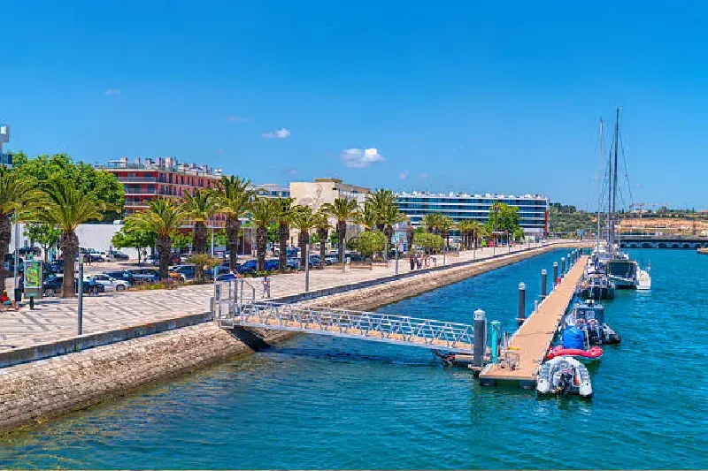 Blick auf die Uferpromenade und den Steg der Lagos Marina an der Algarve, Portugal, mit Booten und ruhigem Wasser