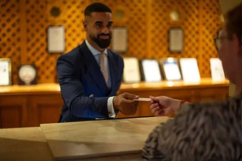 Hotelrezeptionist übergibt einem Gast eine Schlüsselkarte beim Einchecken, während der Reisende seine Ankunft im Hotel vorbereitet. Das Bild zeigt den Empfangsservice und den Beginn eines angenehmen Hotelaufenthalts.