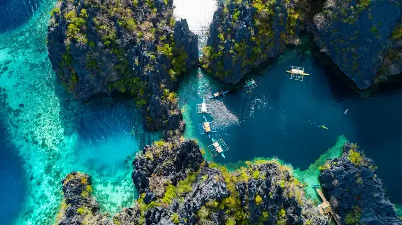 view-of-turquoise-waters-winding-through-dramatic-limestone-cliffs-with-small-wooden-boats-anchored-in-a-secluded-lagoon-in-palawan-philippines