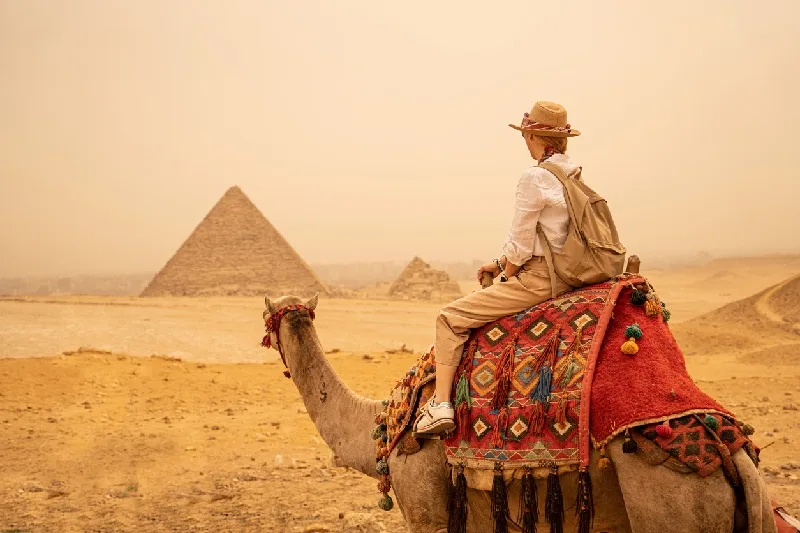 Turista de vacaciones montando en camello frente a las pirámides. Egipto, El Cairo - Guiza.