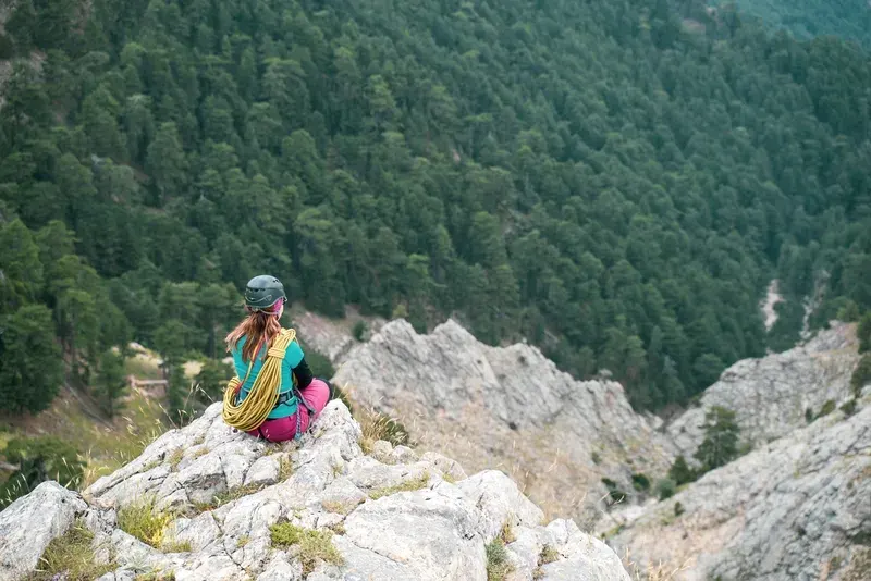 Female mountain alpine rock climber is looking at the view on the peak of a mountain.