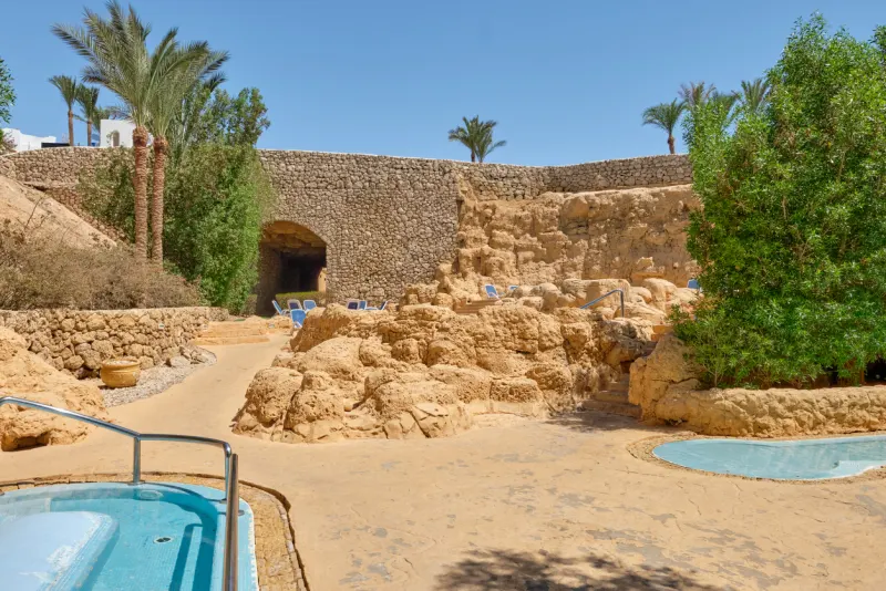 Natural hot spring pools surrounded by rocky formations and palm trees at Cleopatra Bath in Siwa Oasis, Egypt.