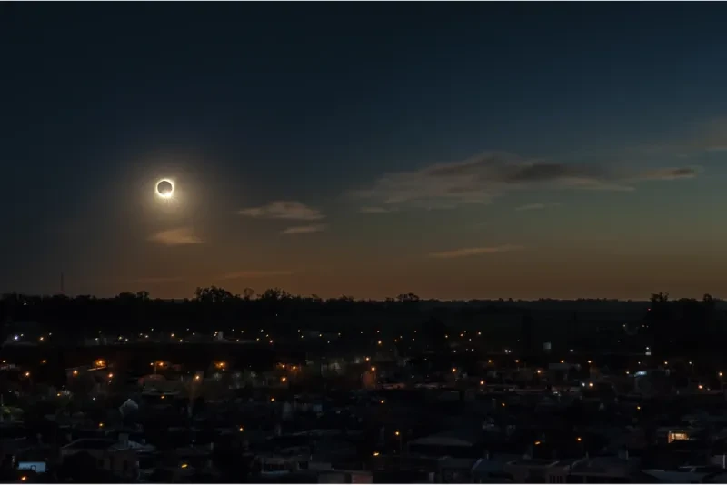 Un eclipse solar total durante la noche sobre una ciudad rodeada de árboles y edificios.