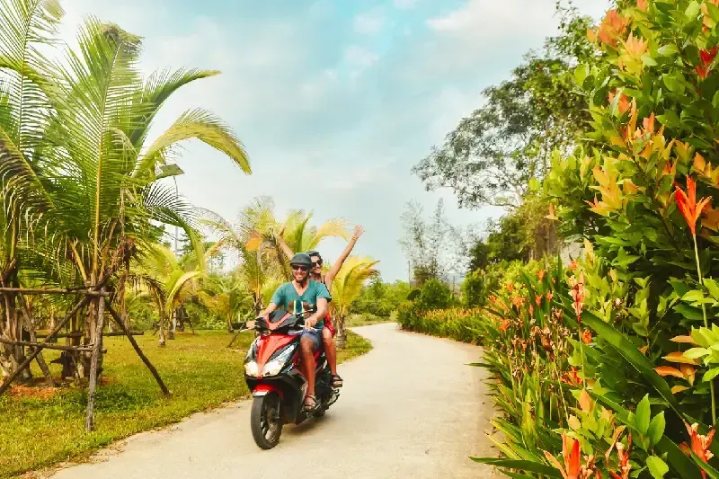 Couple riding motorbike scooter in safety helmets on Phu Quoc island in Vietnam