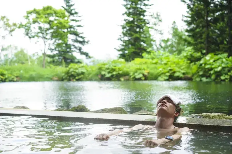 homem-relaxando-em-onsen-ao-ar-livre-cercado-por-natureza-no-japao
