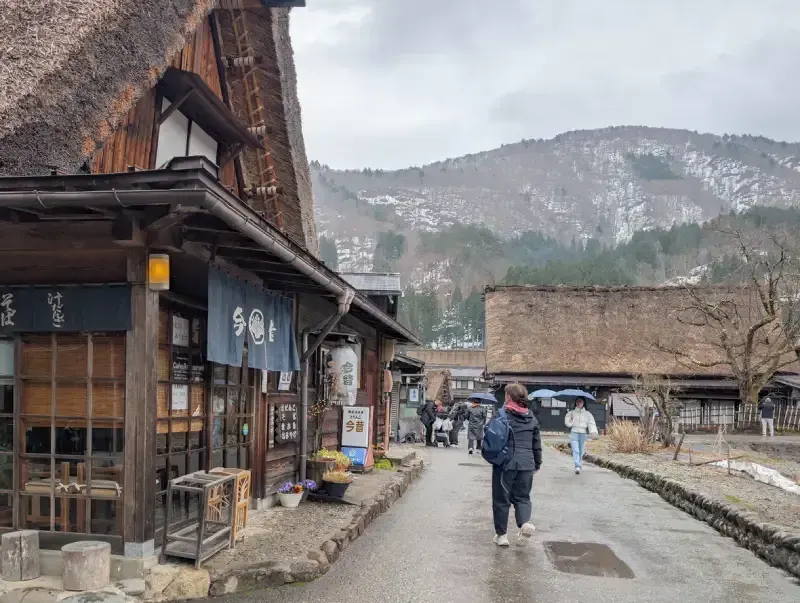 pessoas-caminhando-por-uma-rua-da-vila-de-shirakawa-go-no-japao-cercada-por-casas-tradicionais-de-telhado-de-colmo-gassho-zukuri-e-montanhas-ao-fundo
