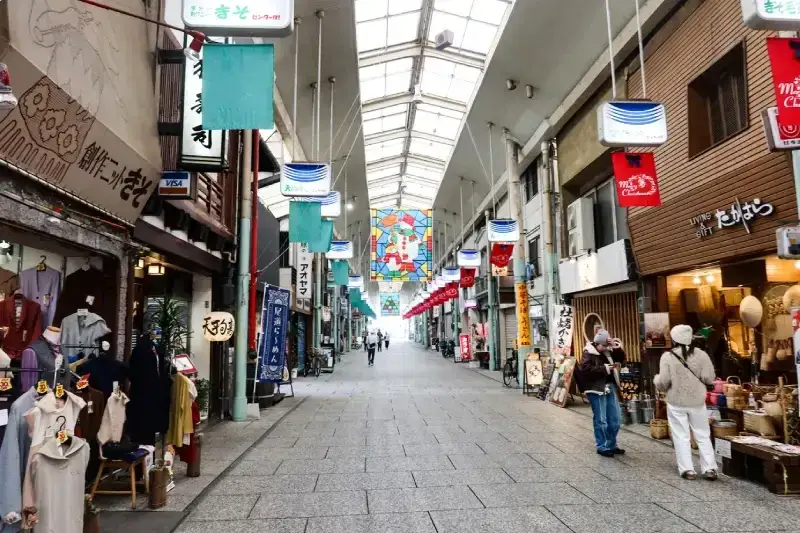 pessoas-caminhando-pela-rua-de-compras-coberta-de-onomichi-no-japao-com-lojas-tradicionais-roupas-expostas-e-bandeiras-coloridas-penduradas-ao-longo-do-corredor
