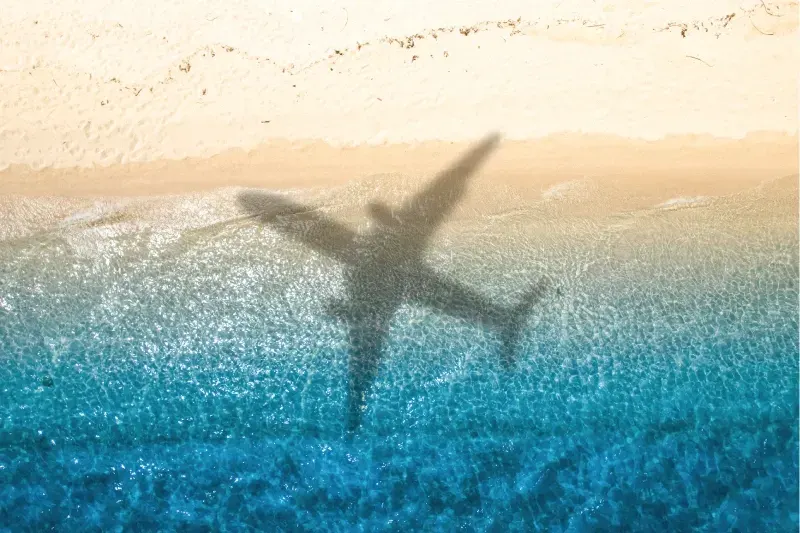 Luftaufnahme eines Passagierflugzeugs als Silhouette über einem Sandstrand mit blauem Meer und Wellen bei Sonnenuntergang – Sommerurlaub und Reisekonzept