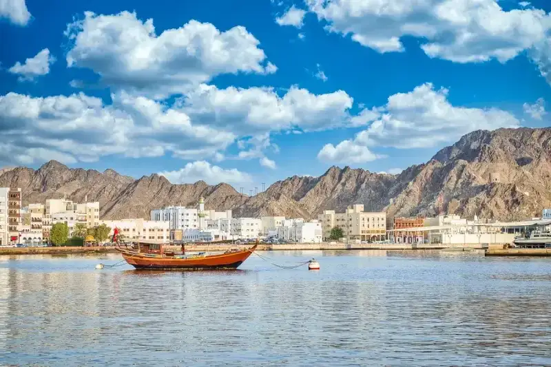 Antica barca a vela ormeggiata alla Corniche di Mutrah. Sullo sfondo si vedono la città vecchia e le montagne. Da Muscat, Oman.