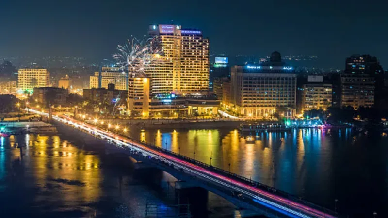 Die Skyline von Cairo bei Nacht mit leuchtenden Gebäuden, spiegelnden Lichtern im Nil und einem lebendigen Stadtbild unter dunklem Himmel.