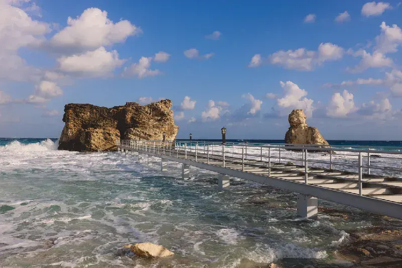 Reihen von Strohdächern mit Sonnenschirmen und Liegen am Sandstrand von Marsa Matruh in Ägypten. Die aufgehende Sonne taucht das ruhige Mittelmeer in warmes Licht und schafft eine entspannte Atmosphäre für einen traumhaften Urlaub.