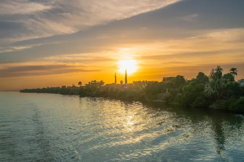 Goldener Sonnenuntergang über dem Nil in der Nähe der Esna-Schleuse mit Minarett und Palmen.
