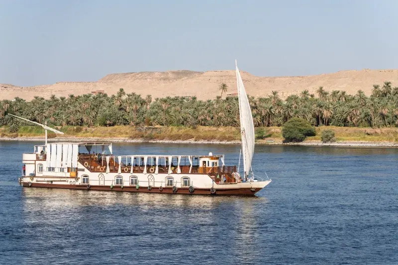 La nave da crociera Dahabiya Nile naviga lungo un deserto sabbioso con palme sul fiume Nilo vicino ad Assuan