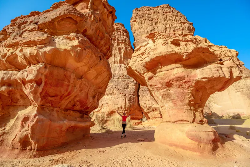 Mujer con los brazos extendidos entre impresionantes formaciones de arenisca en el desierto de AlUla, Arabia Saudita.