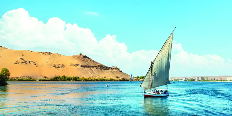 Traditional felucca sailing on the Nile River in Aswan under a blue cloudy sky.