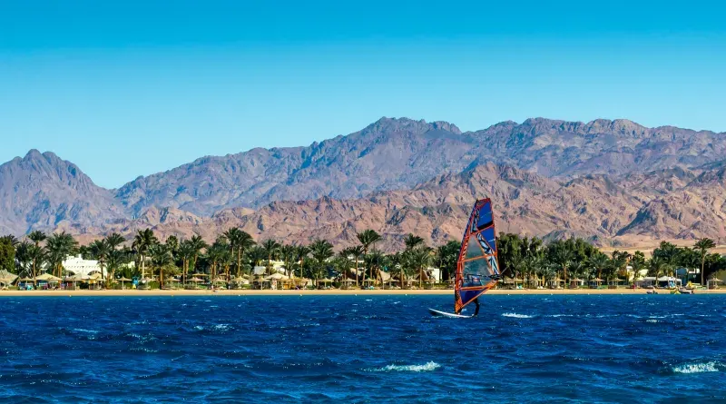 Windsurf no mar com palmeiras e montanhas ao fundo, Dahab, Egito.