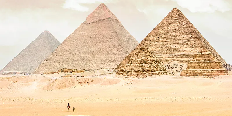 The iconic Pyramids of Giza stand majestically in the vast sandy desert under a dramatic cloudy sky, symbolizing ancient Egyptian civilization and a world-renowned travel destination.