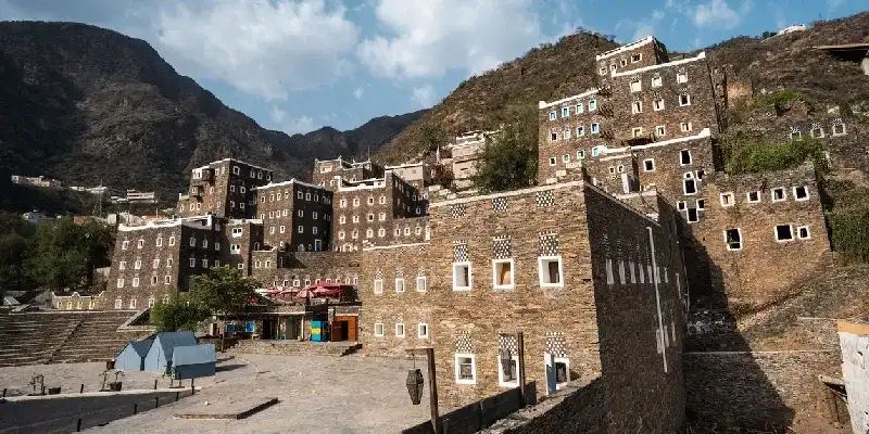 Vista panorámica de los edificios tradicionales de piedra de Rijal Almaa, rodeados de montañas bajo un cielo azul despejado.