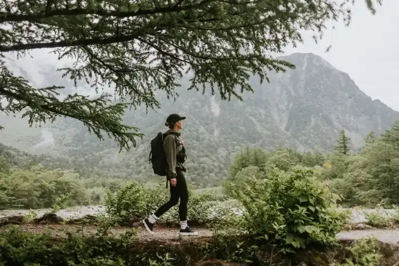 mulher-com-mochila-caminhando-por-uma-trilha-em-kamikochi-com-montanhas-dos-alpes-japoneses-ao-fundo-cercadas-por-vegetacao-densa-e-neblina