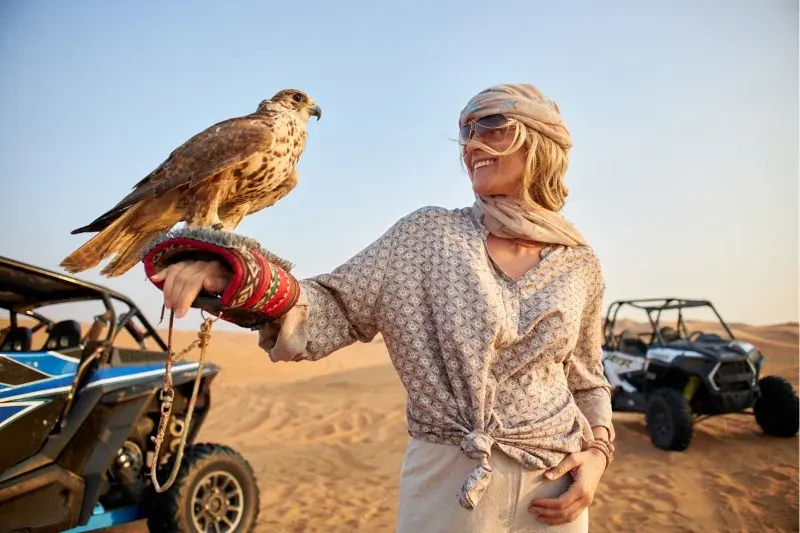 Bella donna nel deserto di Dubai che tiene un falco in braccio, atmosfera da vacanza.