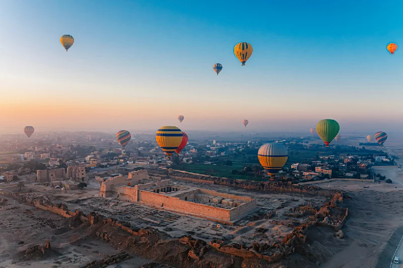 Vista aérea al amanecer de coloridos globos aerostáticos flotando sobre las antiguas ruinas de Medinet Habu.