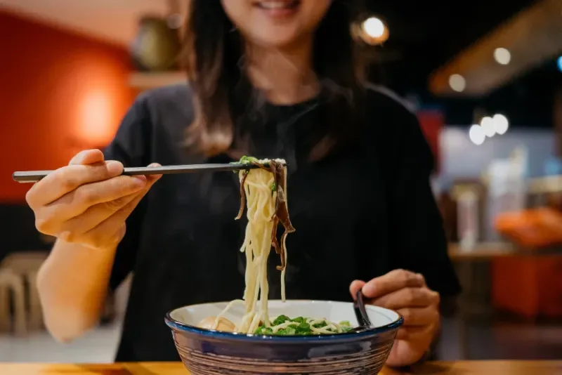 Mujer asiática comiendo un tazón de ramen japonés con palillos en un restaurante de ramen japonés.