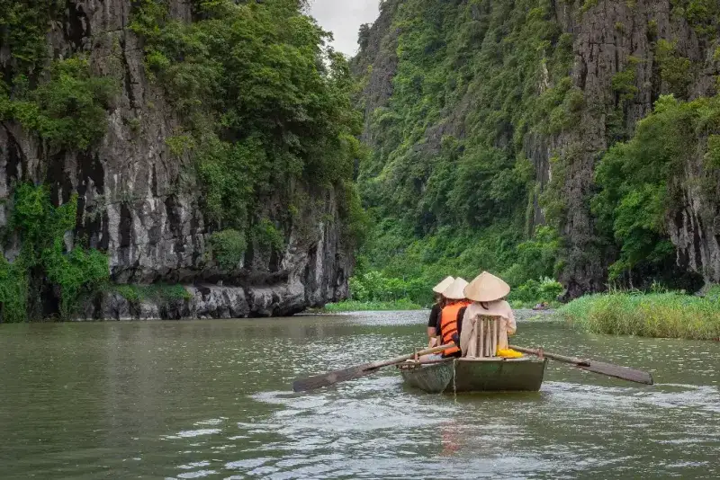 Personas en un bote que desciende por un río rodeado de exuberantes bosques tropicales y montañas, Tam Coc Ninh Binh, Vietnam.
