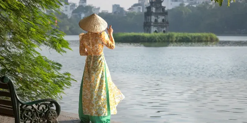 Mujer con traje tradicional vietnamita y sombrero cónico en el lago Hoan Kiem en Hanói, Vietnam.