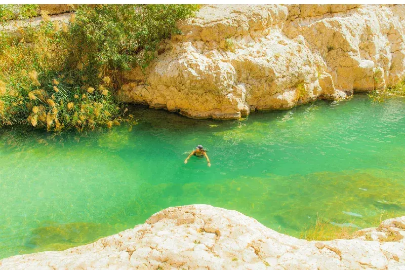 female traveller admiring swimming in bright green rivers of Wadi Ash Shab canyon