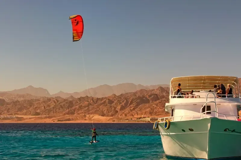 Un kiteboarder si diverte a fare surf nelle acque azzurre del Mar Rosso, vicino a uno yacht ormeggiato, lungo la penisola del Sinai in Egitto.
