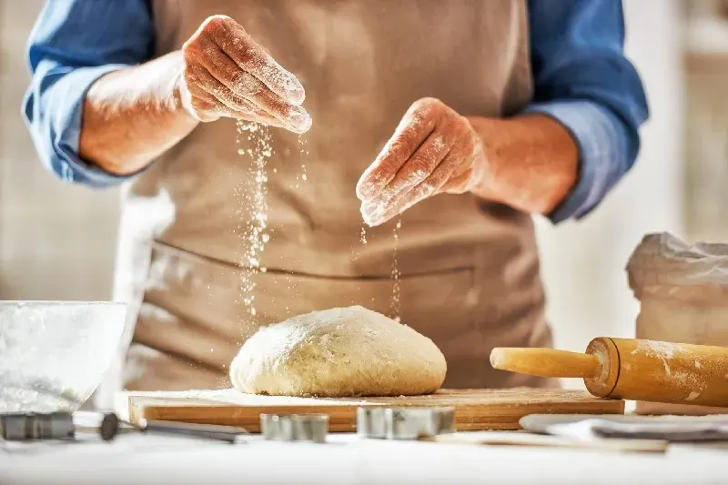 Nahaufnahme eines Bäckers bei der Arbeit. Selbstgemachtes Brot. Hände bereiten Teig auf einem Holztisch zu.