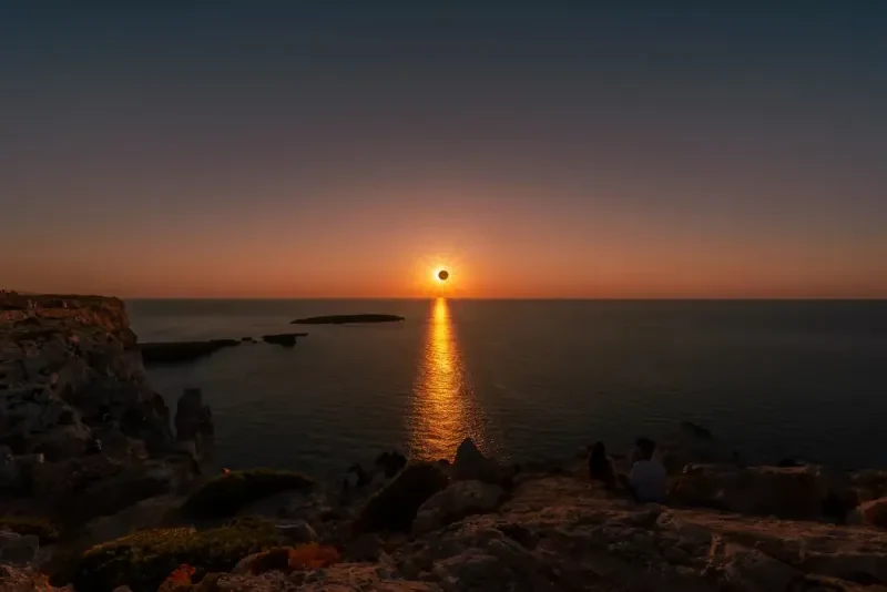 Eclissi solare sul mare, vista da una costa rocciosa, con il Sole parzialmente oscurato dalla Luna.