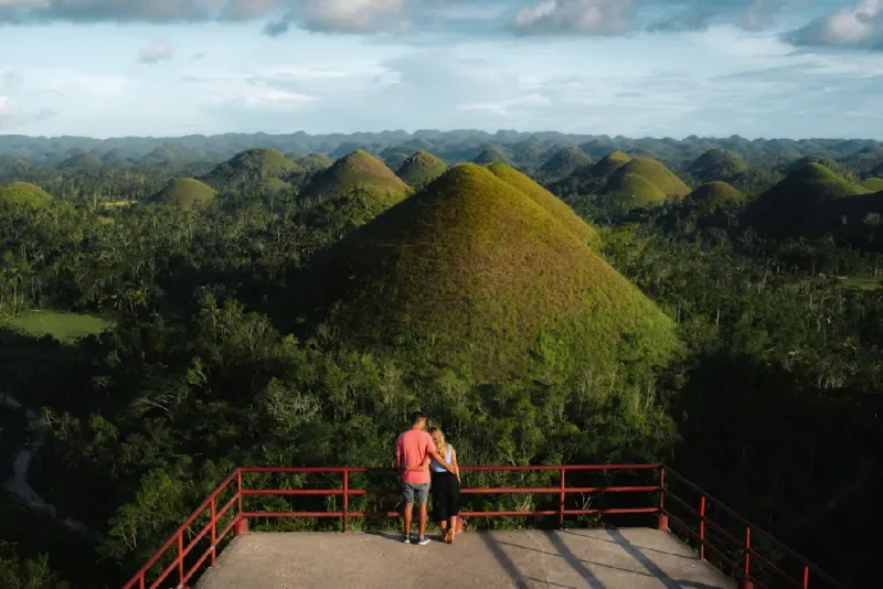 Panoramic view of the Chocolate Hills in Bohol, Philippines, with visitors overlooking the unique cone-shaped hills.