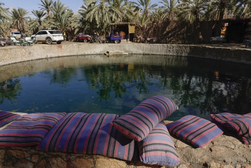 Cleopatra's Bath in Siwa Oasis, Egypt, featuring a crystal-clear natural spring surrounded by palm trees and traditional seating.