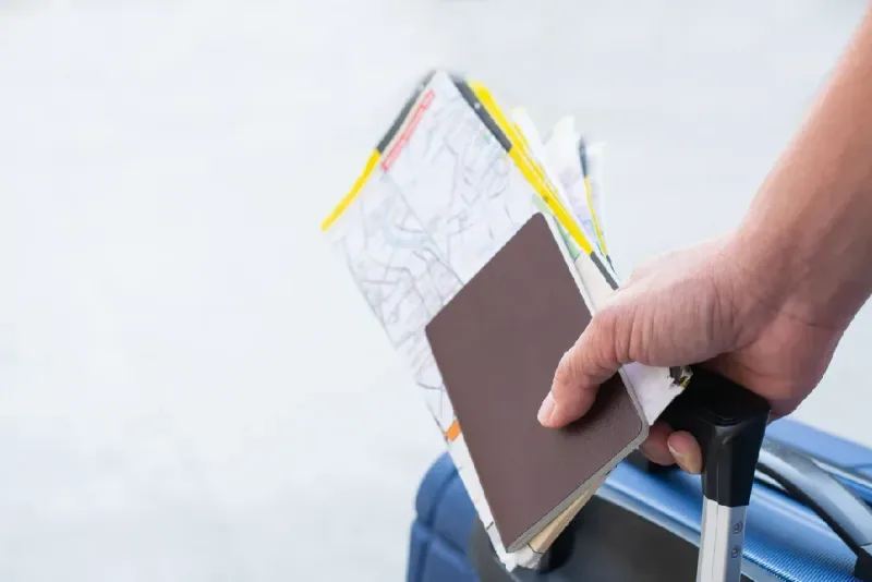 Viajero sosteniendo pasaportes y un mapa de viaje junto al equipaje para su aventura.