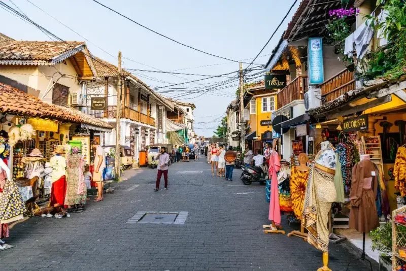 La gente camina entre edificios históricos decorados con letreros de tiendas en una calle estrecha del Fuerte de Galle.