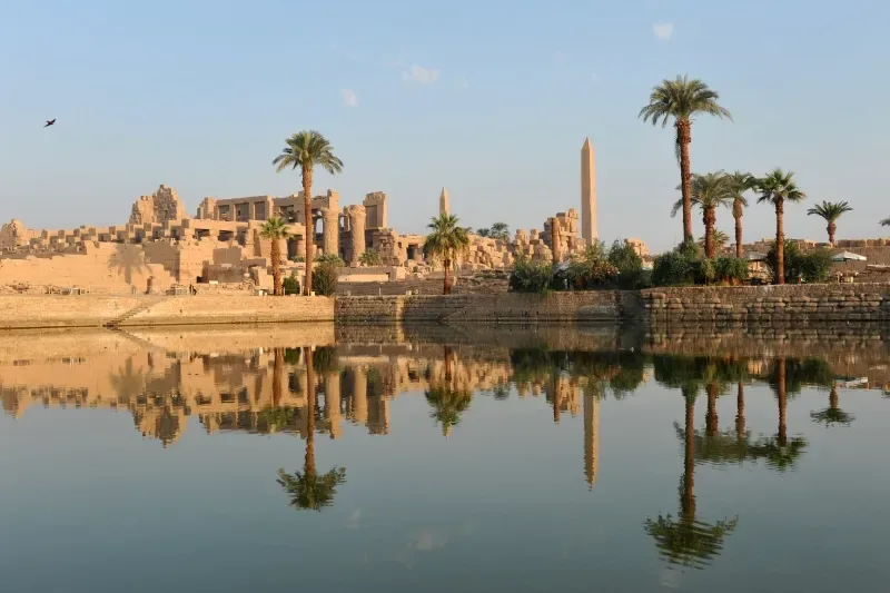 Panorama del Karnak con palme e antiche rovine che si specchiano nell'acqua immobile in Egitto.
