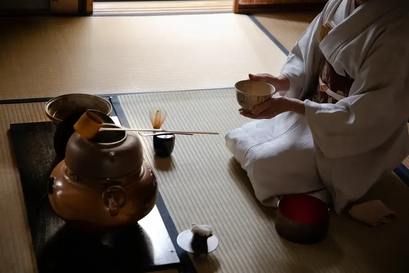 mulher-em-quimono-segura-tigela-de-matcha-com-as-duas-maos-ajoelhada-em-sala-de-tatame