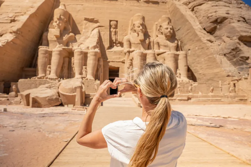 Tourist making a heart shape with her hands while admiring the Abu Simbel Temples in Aswan, Egypt.